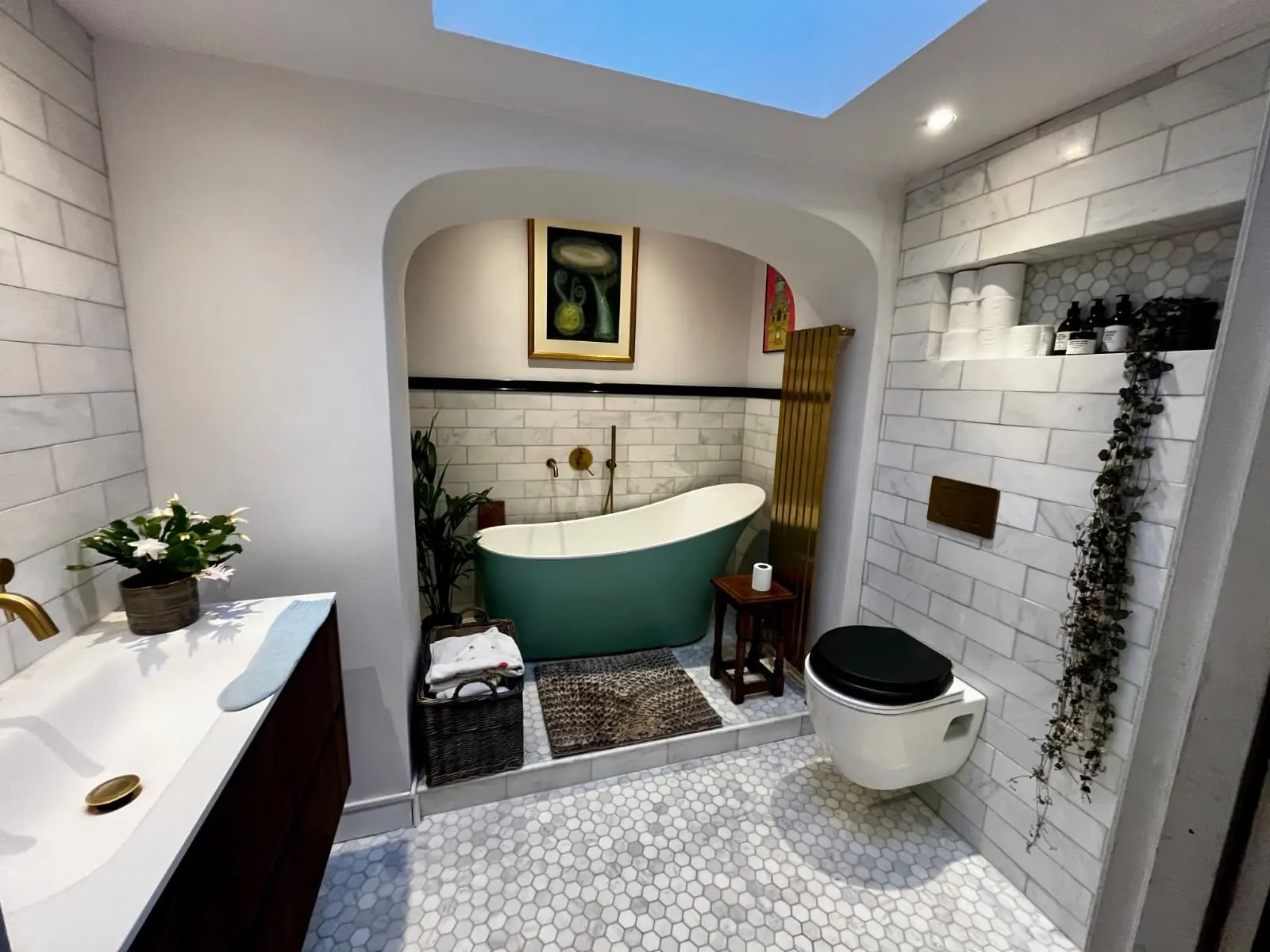 Finished bathroom with a green slipper bath in an arched alcove, brass radiator, marble metro tiles and hexagon marble floor, by PT Renovations