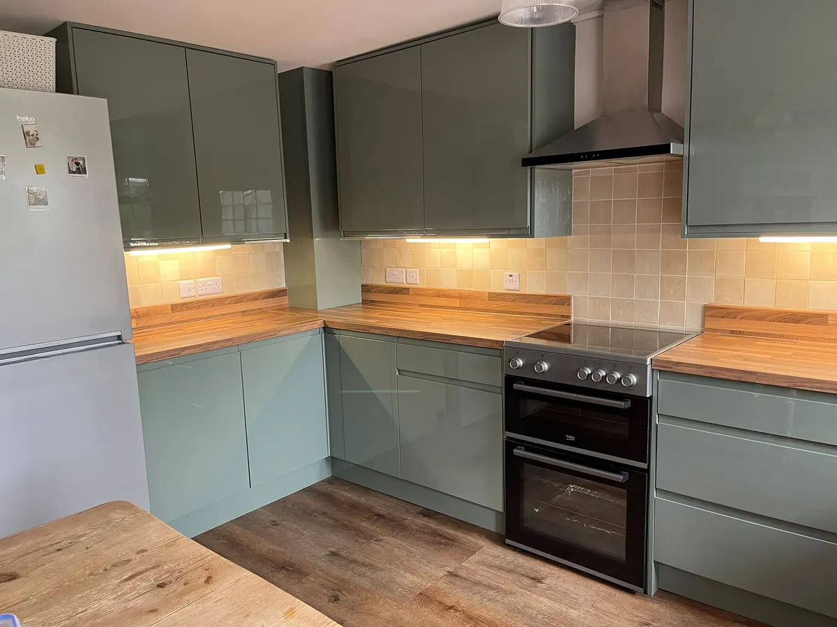 After: sage green gloss handleless kitchen with under-cabinet lighting, wood-effect worktops and LVT floor