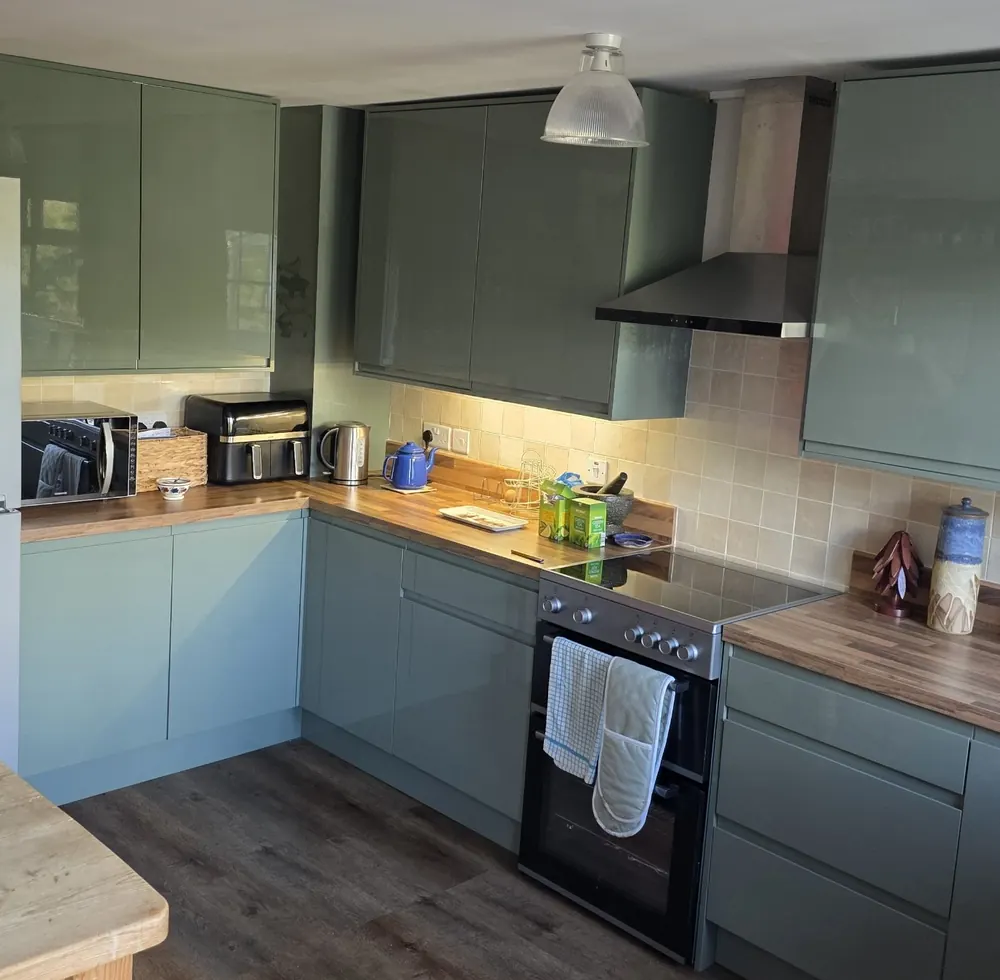 New L-shaped sage green gloss kitchen with wood-effect worktops, under-cabinet lighting and LVT flooring, fitted by PT Renovations