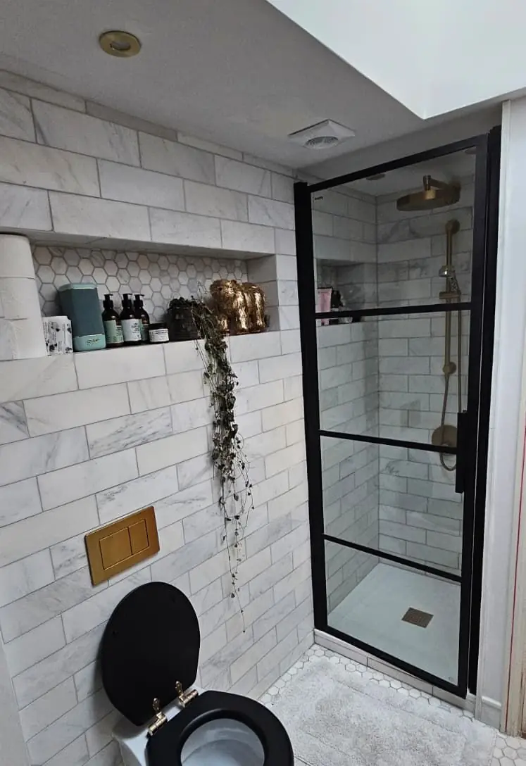 Walk-in shower with black-framed screen, brass fittings and marble metro tiles