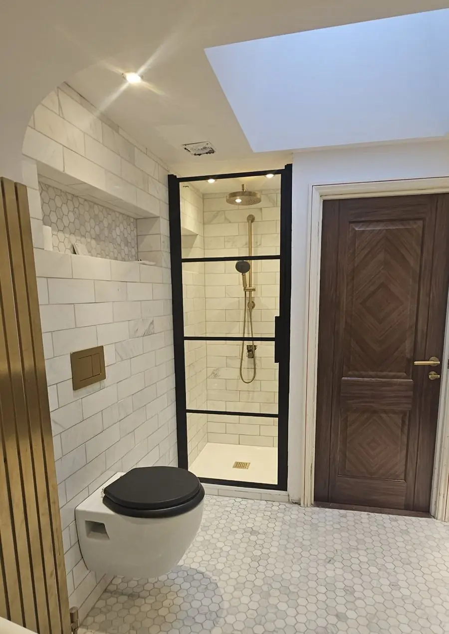 Bathroom with a black-framed shower screen, brass shower and marble metro tiles