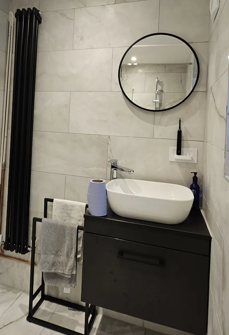 Wall-hung vanity with a countertop basin, round mirror and black column radiator